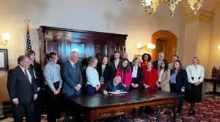 people standing around a desk while someone signs a paper