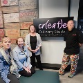 group of people standing in front of the museum create culinary studio sign