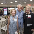 Three people posing at the event with others mingling in the background
