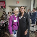 Two women posing while others find their seats for the program