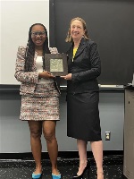 A picture showing two women standing in front of a projector screen holding a plaque.