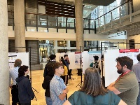 A picture of 6 academic poster hangers with research posters on them. a group of people stand in the foreground discussing.