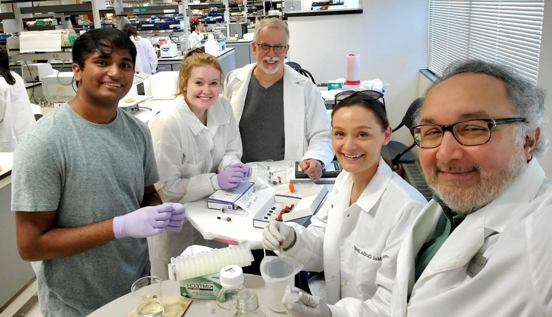 Image of Dr. Menon with students in a lab